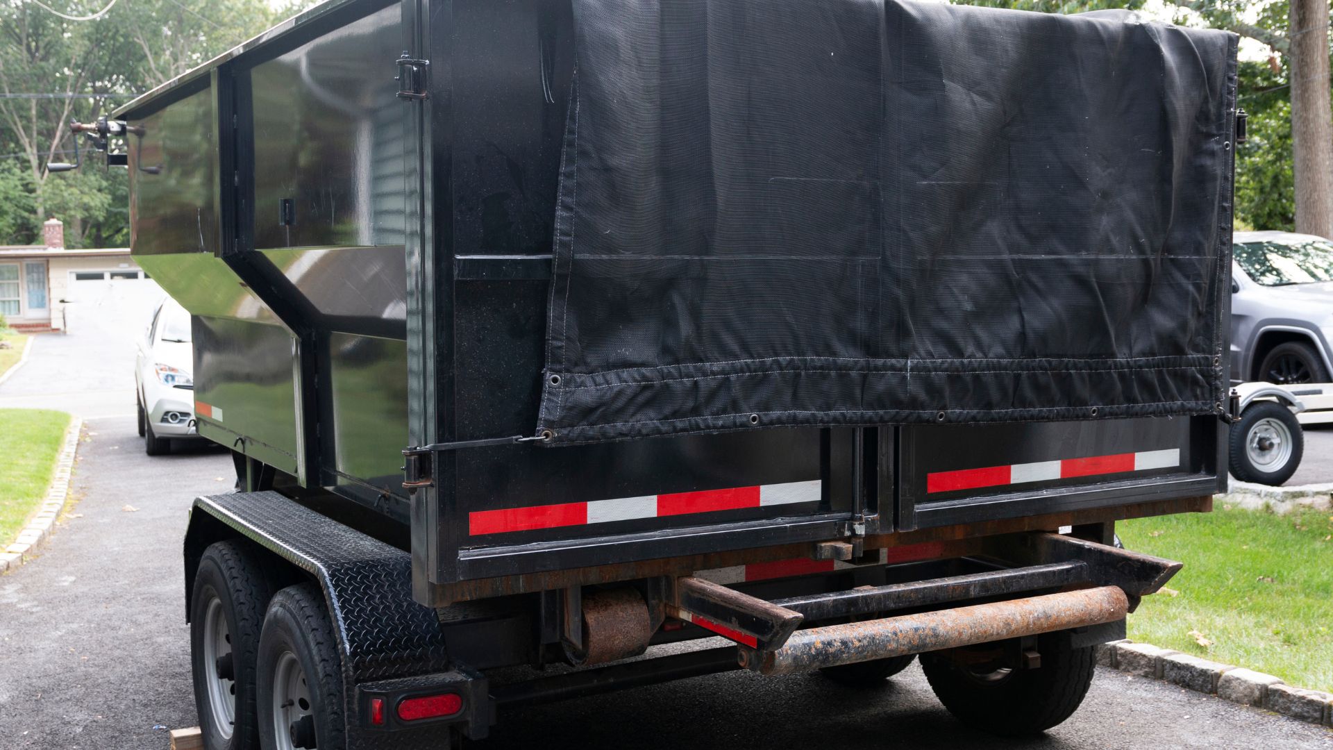 Black dump trailer with covered top parked on residential street