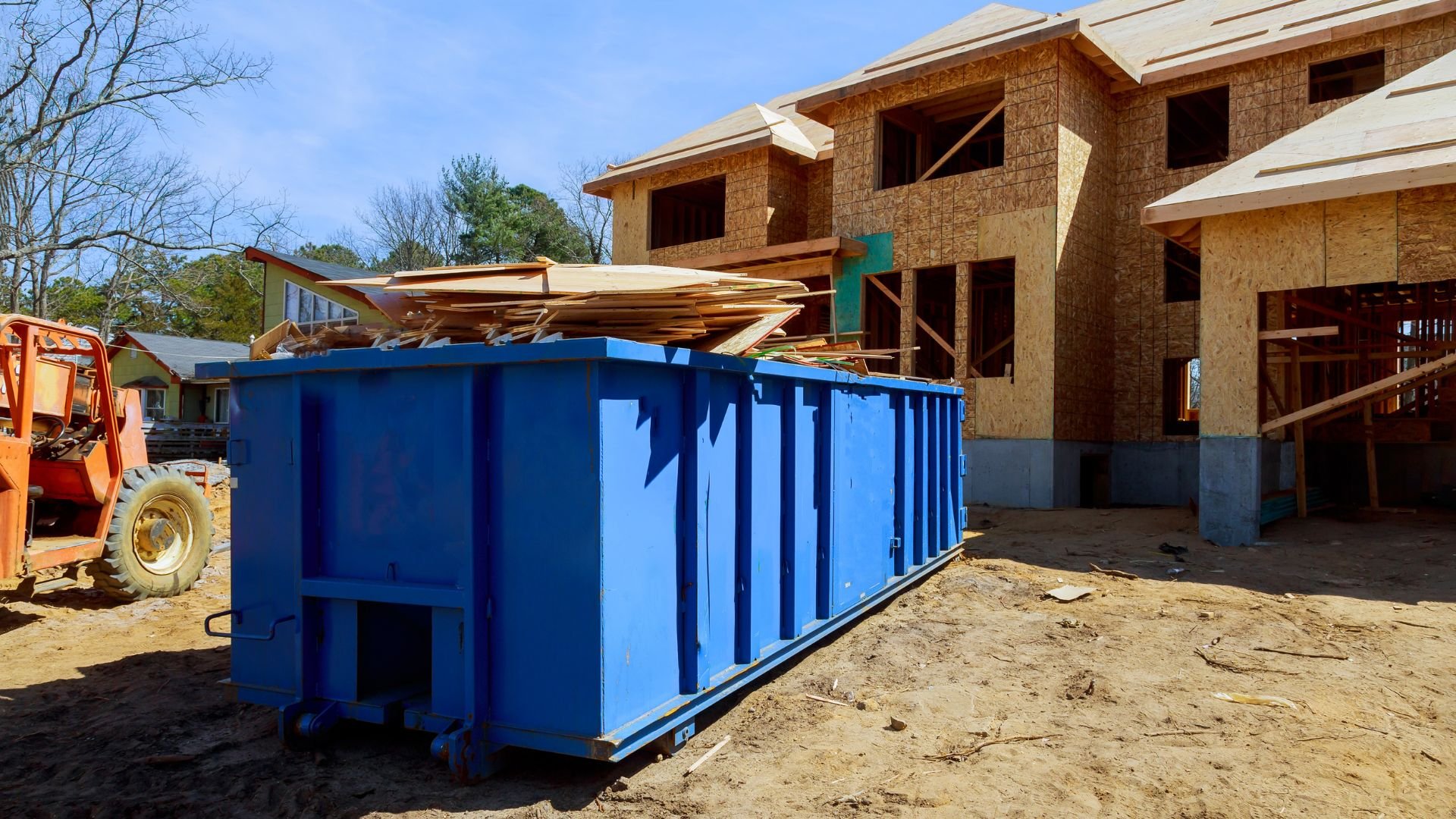 Blue dumpster at construction site with wooden house framing in background