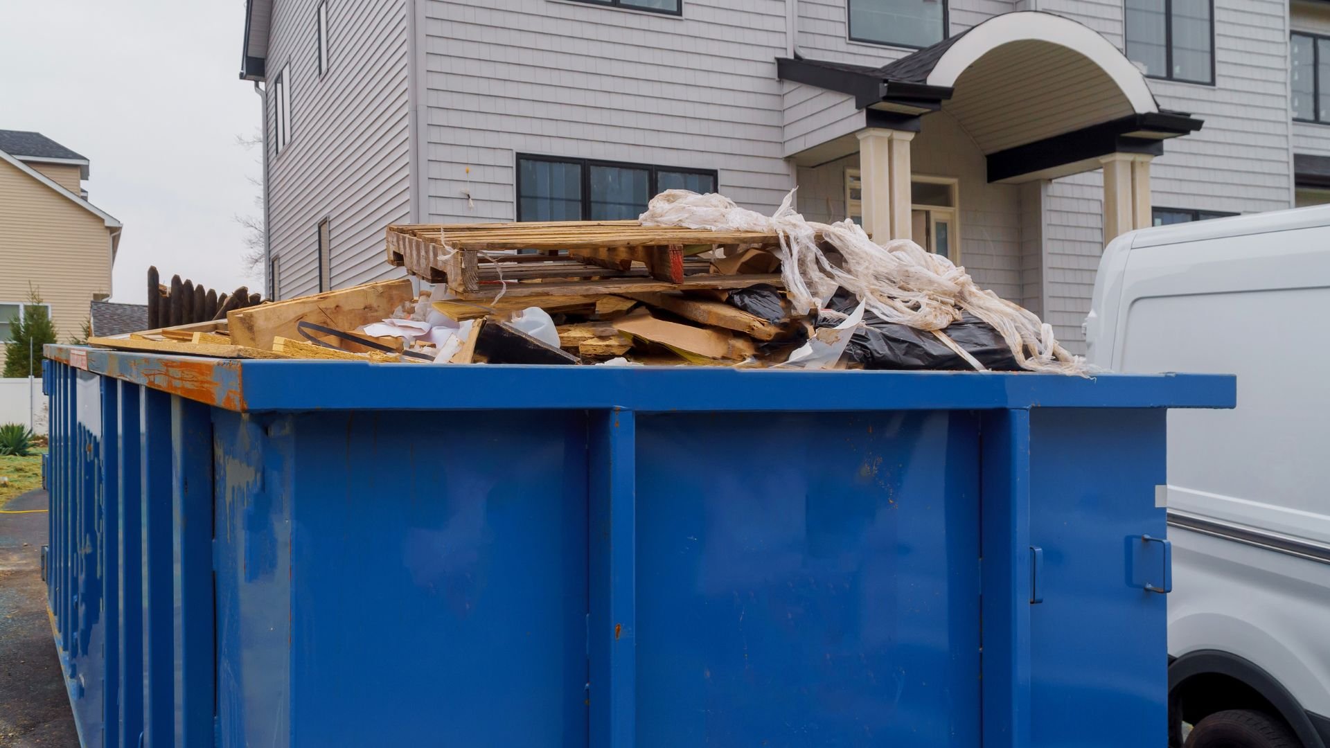 Blue dumpster filled with wooden debris near residential construction site