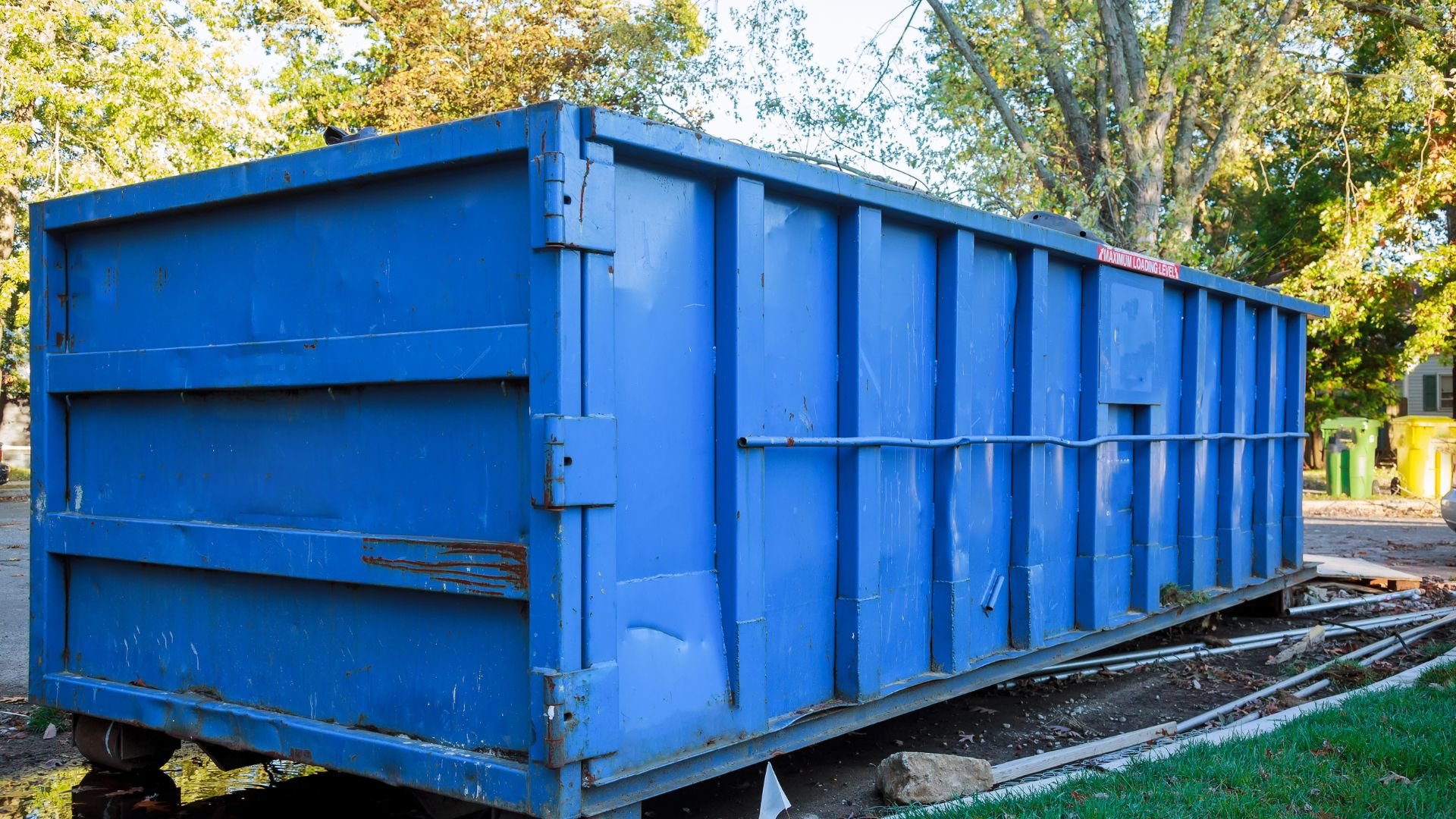 Large blue dumpster in suburban setting with trees and grass