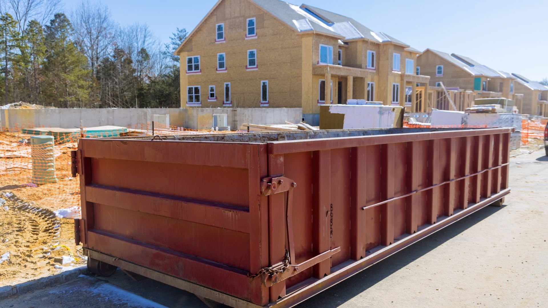 Large red dumpster at residential construction site with new houses