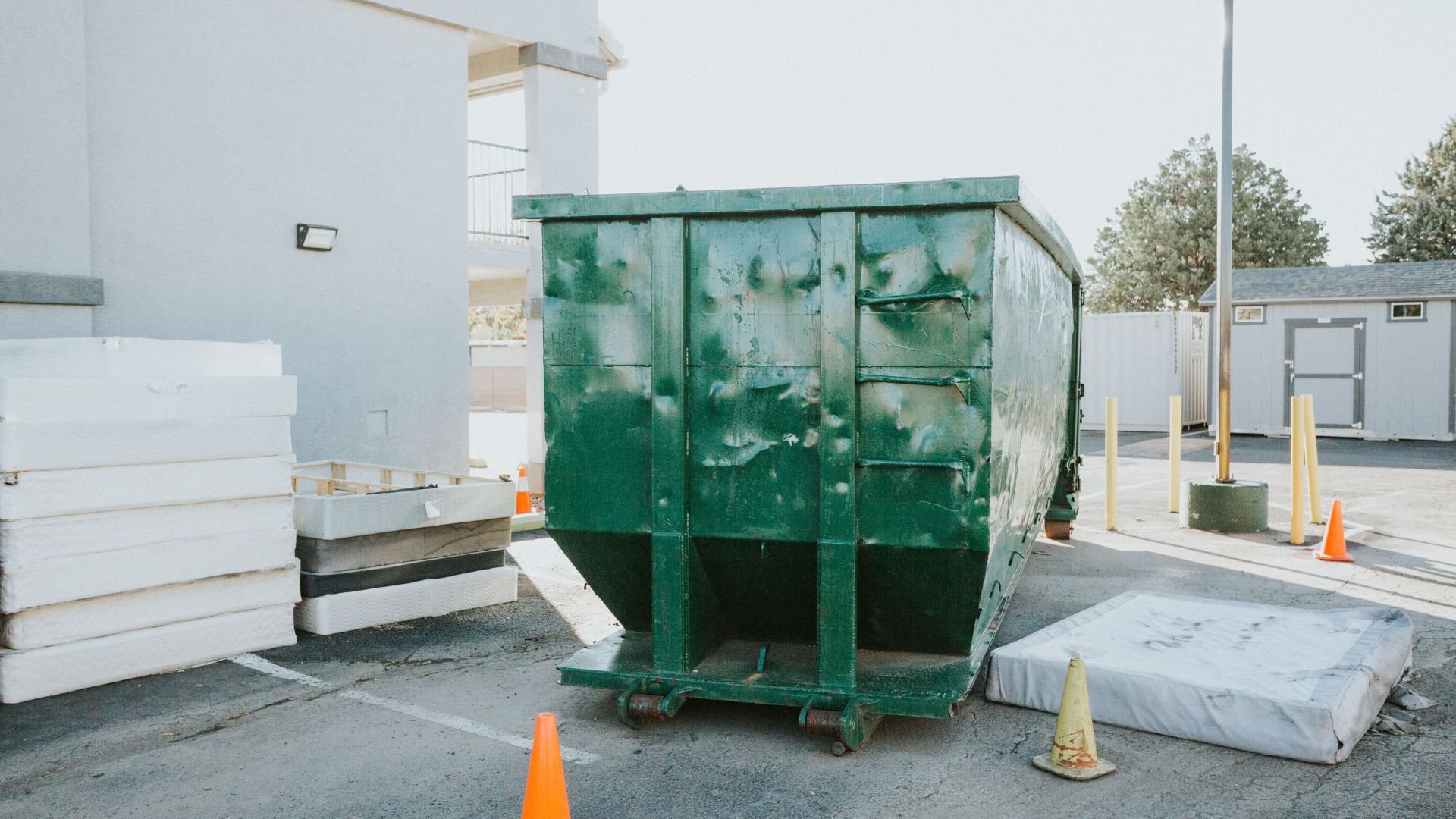 Large green dumpster with orange safety cones in industrial parking lot