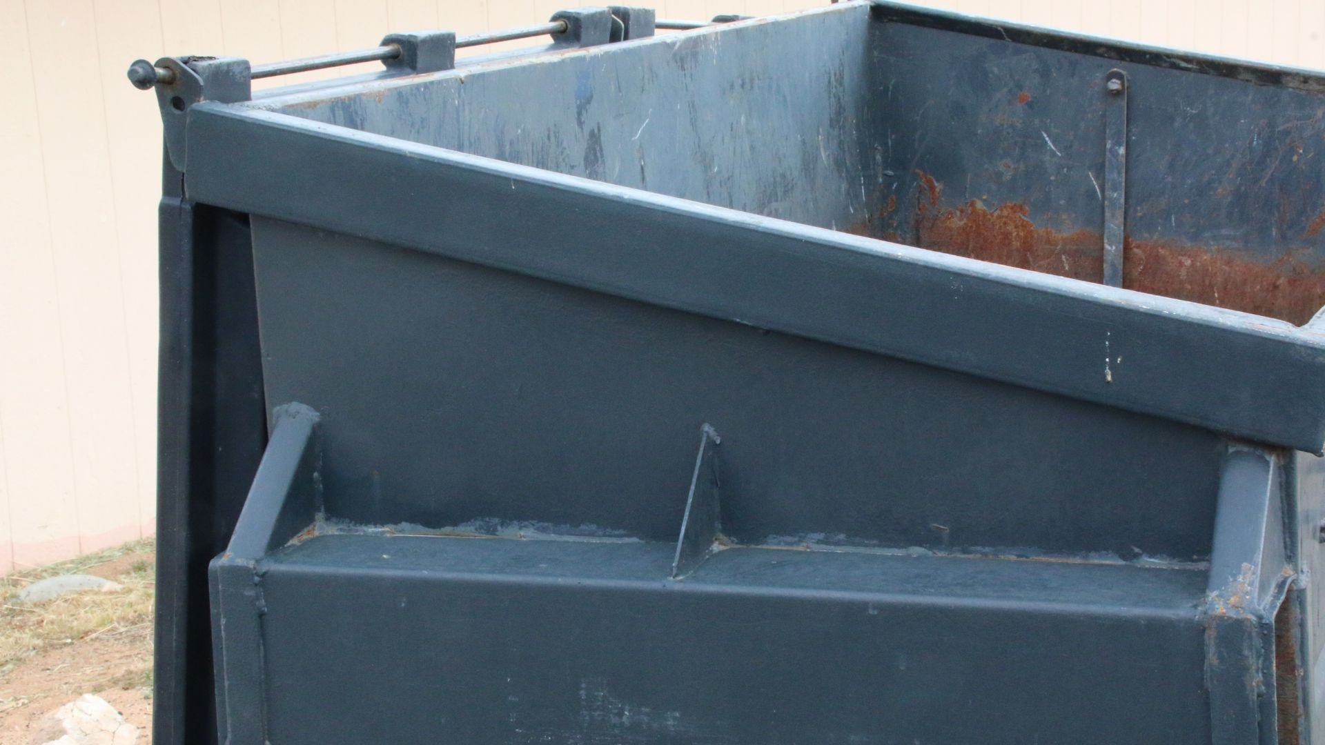 Large blue-gray industrial dumpster with rust marks and metal hinges