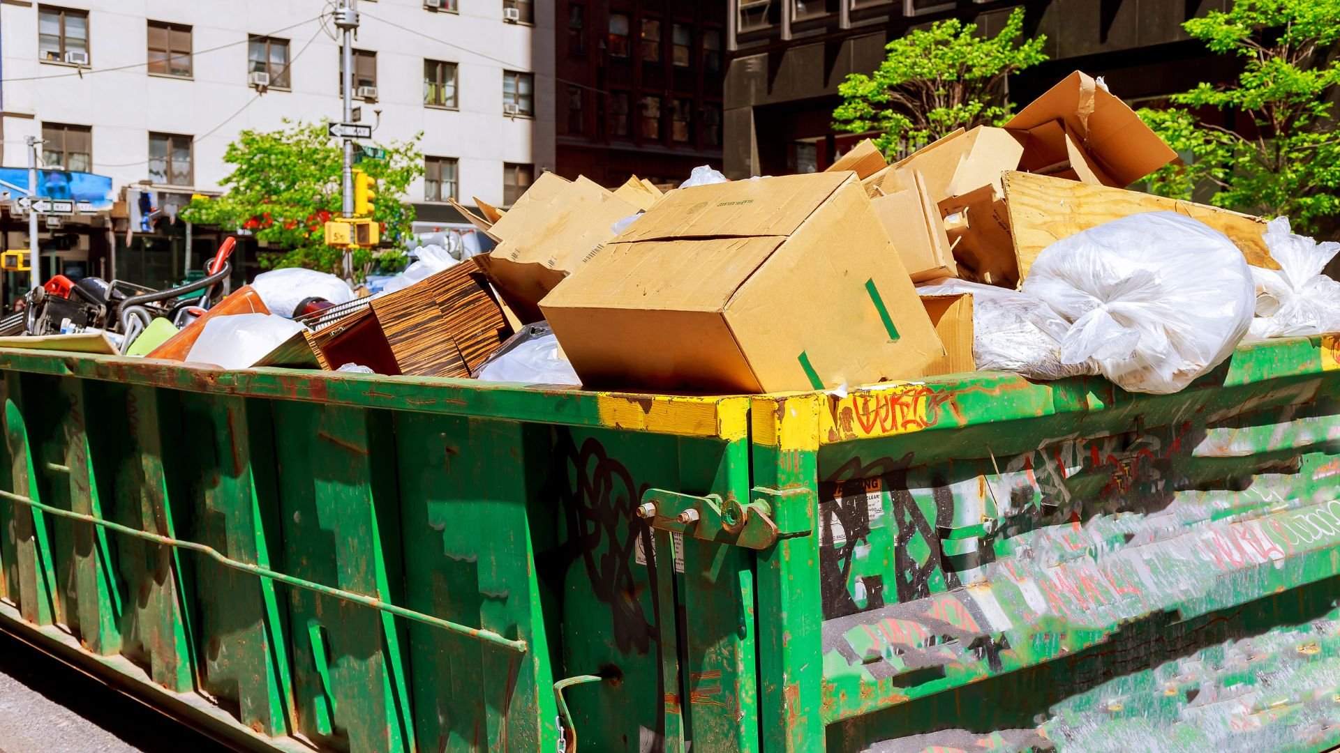 Overflowing green dumpster filled with cardboard boxes in urban setting