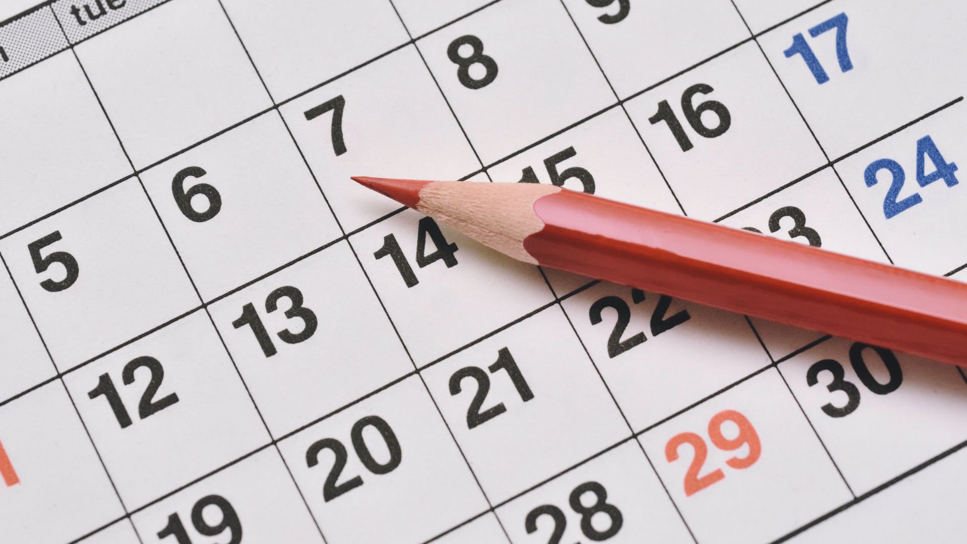 Red pencil resting on a monthly calendar showing dates and numbers