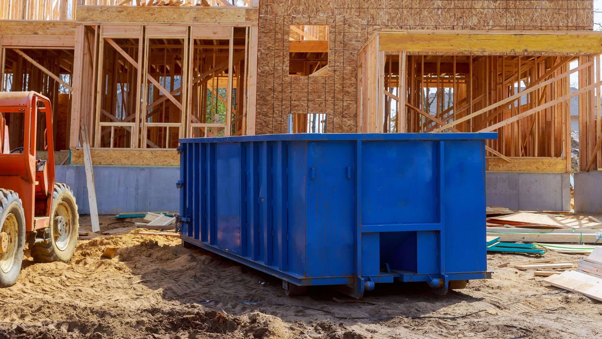 Blue dumpster at construction site with wooden framed building in progress