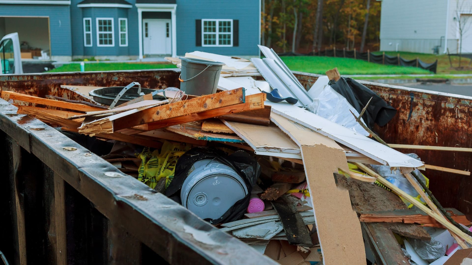 Rusty dumpster filled with construction debris near blue house