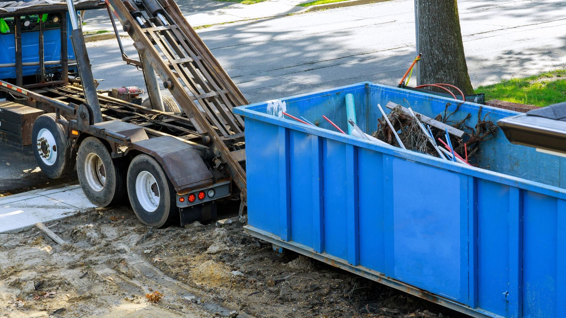 Blue dumpster and truck on construction site with debris and soil