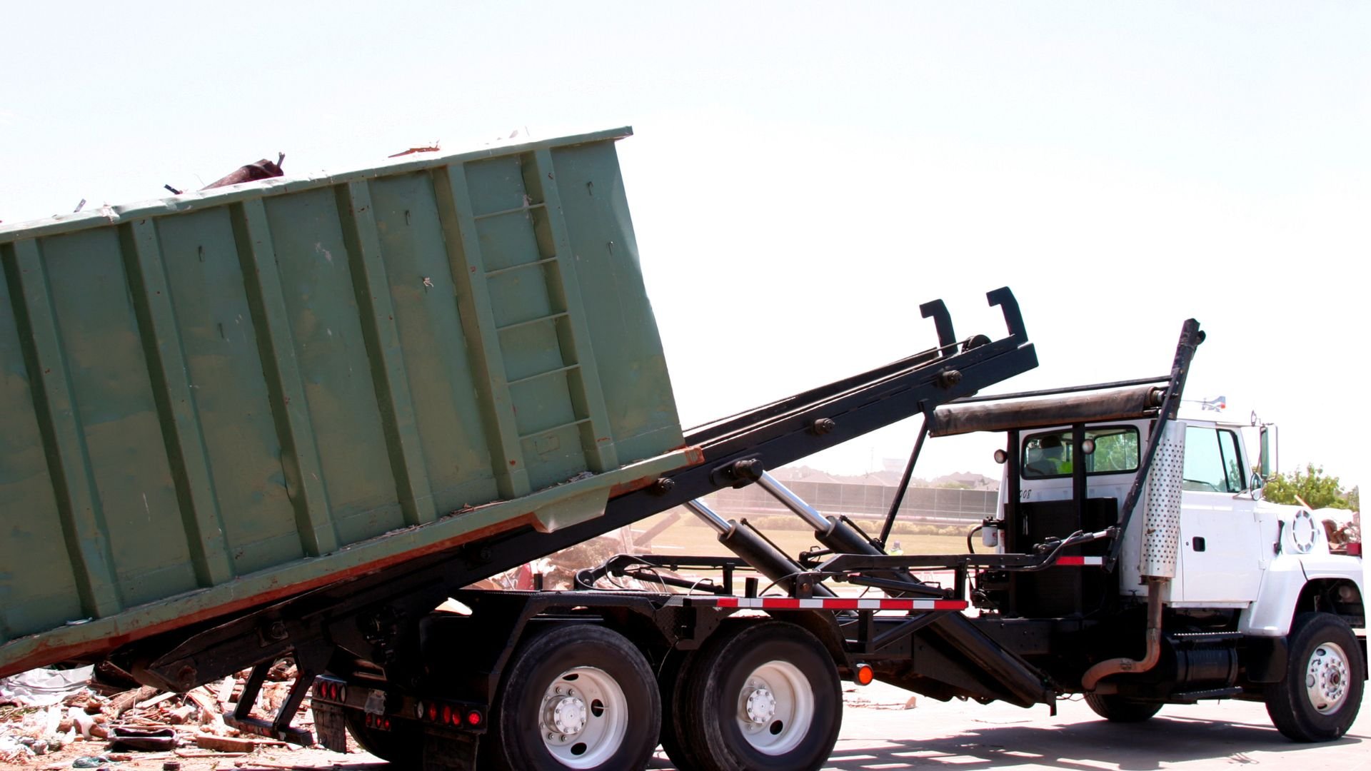 White truck lifting large green dumpster at construction or demolition site