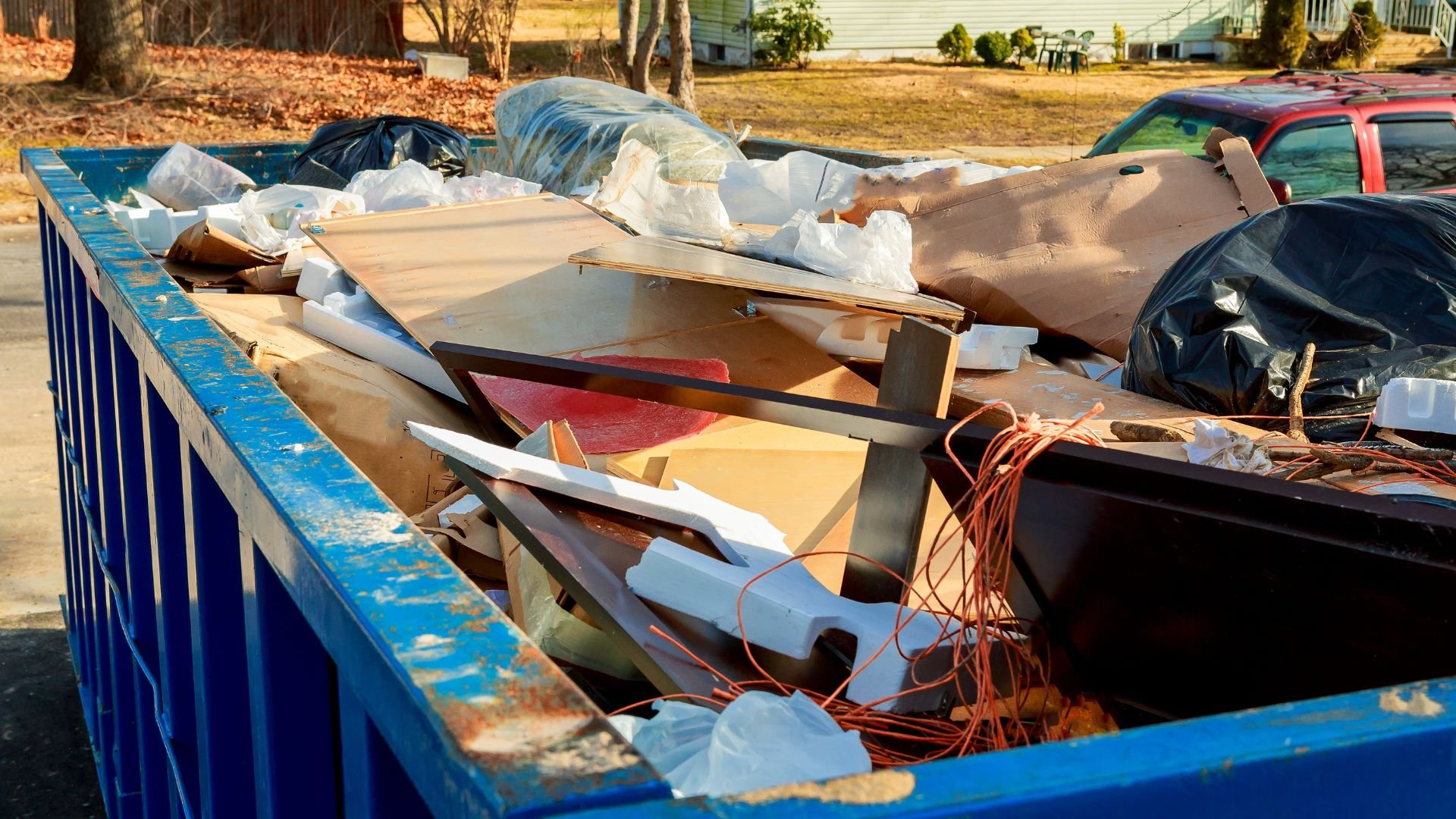 Blue dumpster filled with construction debris and trash in residential area