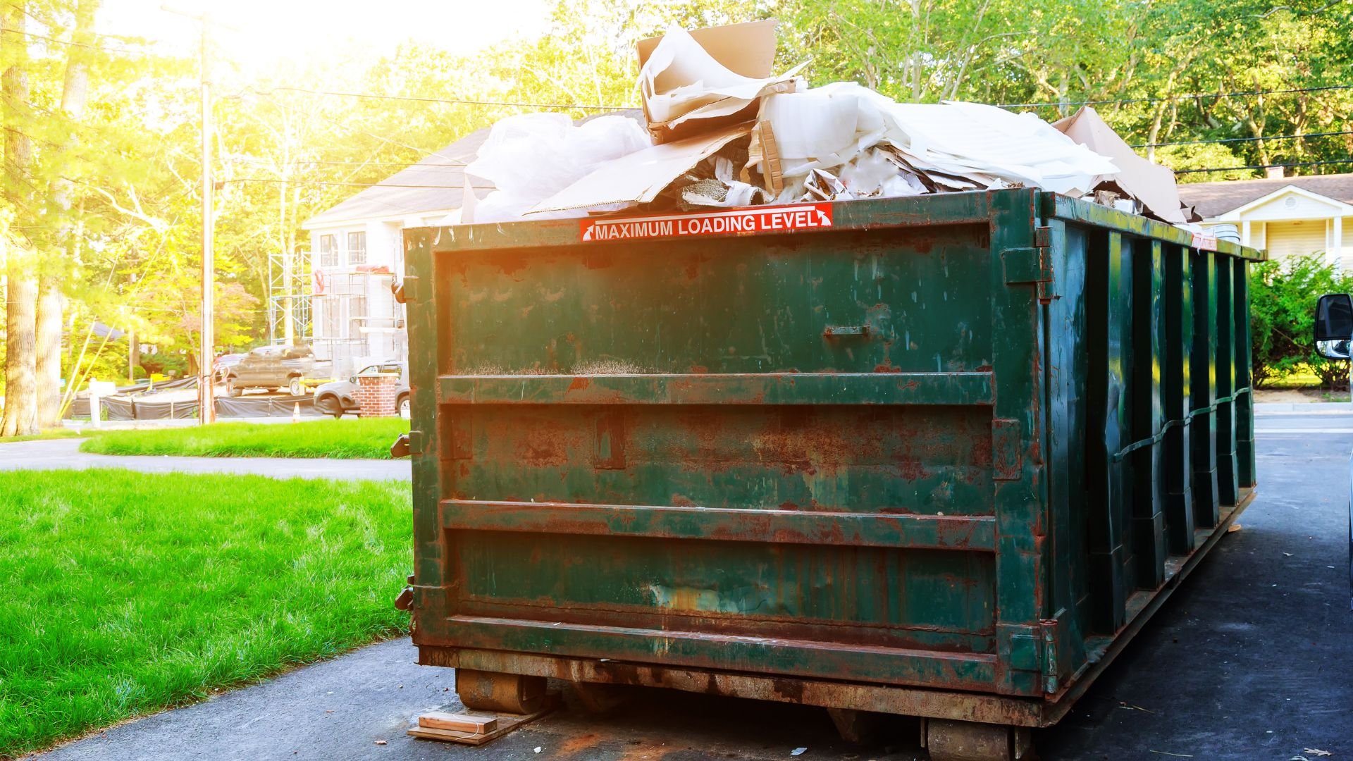 Large green dumpster filled with debris on residential street