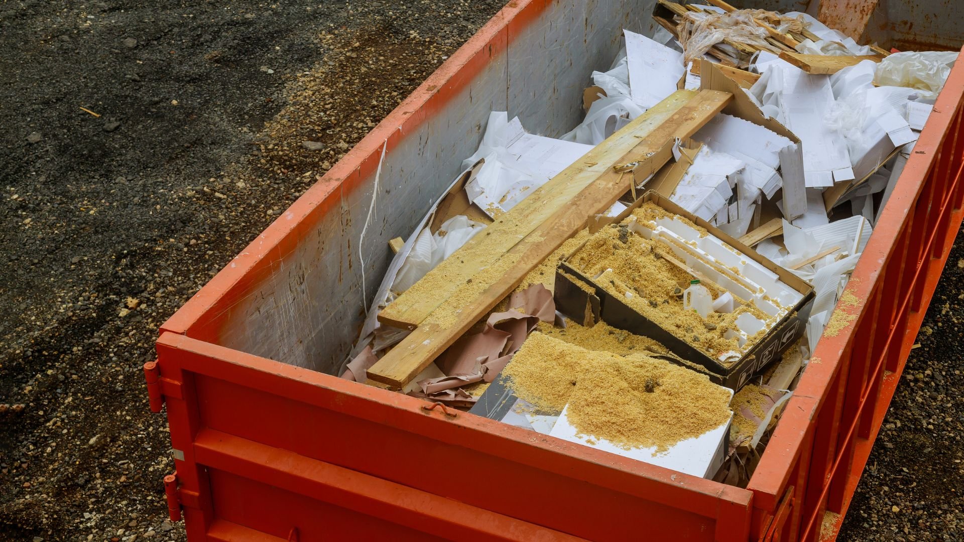 Red construction dumpster filled with wood, paper, and sawdust debris